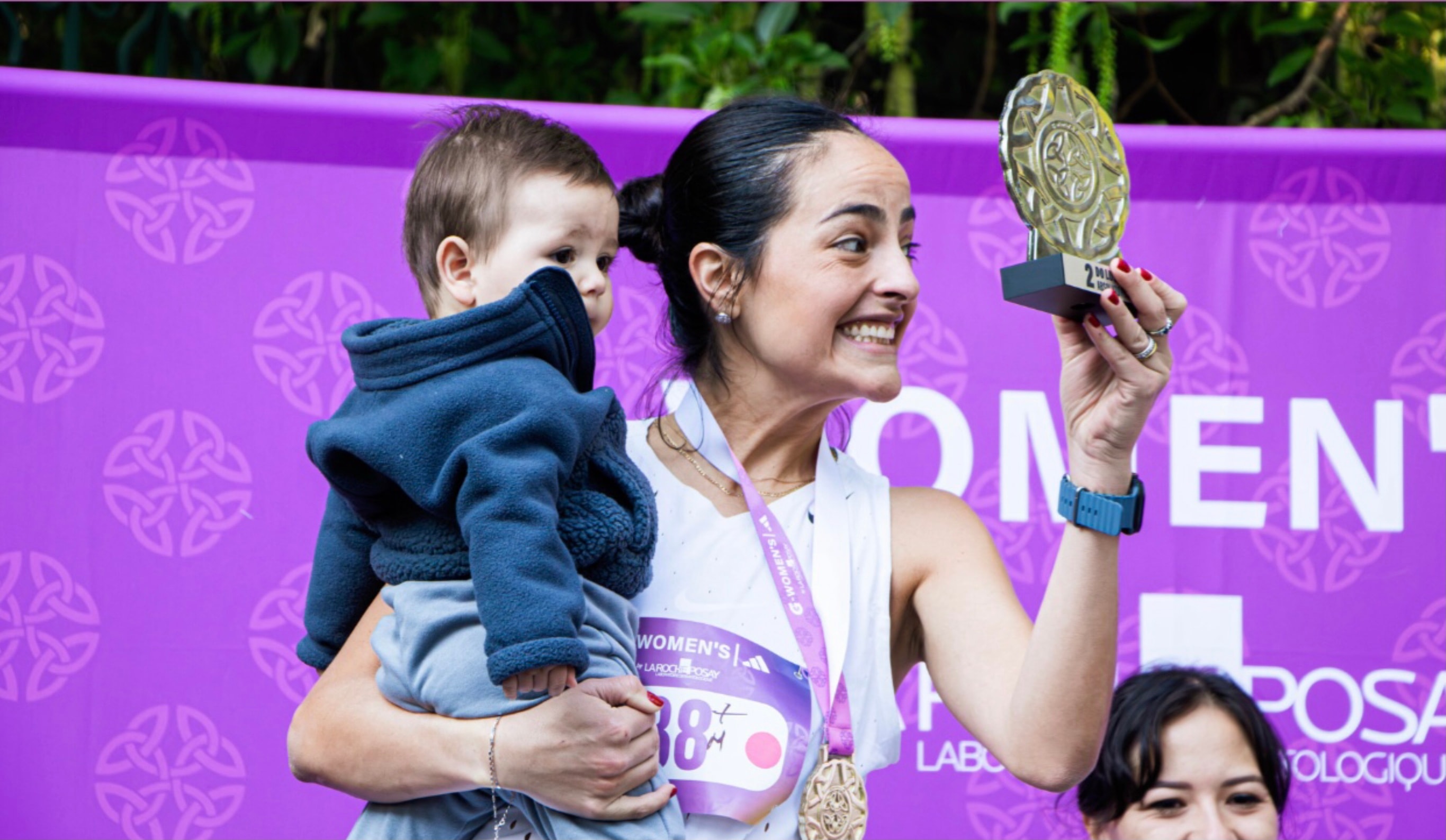 G-Women's Ten K — atleta con trofeo y bebé